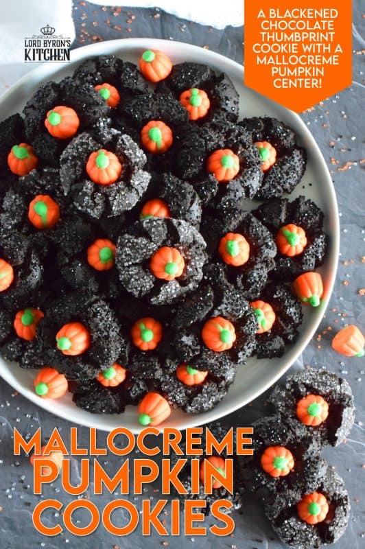 These festive cookies are deliciously decadent. The base is a chocolate cookie that has been darkened to resemble the blackness that goes hand in hand with Halloween. Before baking, the cookie is rolled in black sanding sugar which adds a glistening effect. Finally, a Mellocreme Pumpkin is pushed into the center to make these one of the most adorable Halloween cookies! #halloween #mellocreme #pumpkin #cookies #candy #candycorn