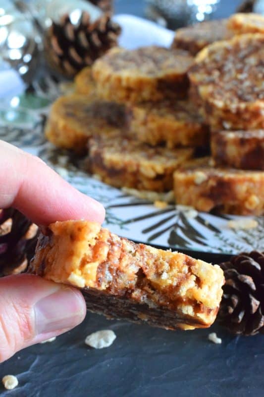 Caramel Peanut Slices are a no-bake confection consisting of caramel, peanut butter, rice krispies cereal, chocolate, and chopped peanuts. Working in layers, it is rolled into a log and chilled until set. The log is cut into slices before being served. These cookies are irresistible and one of my all-time favourite Christmas treats! #caramel #caramellogs #christmas #holiday #nobake #cookies #peanutbutter
