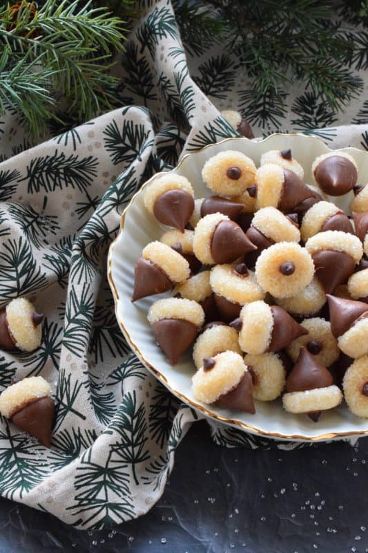 These adorable bite-sized cookies are bound to be a complete hit! They look stunning all on their own, but are perfect for filling in the gaps on your Christmas cookie platter. Hershey Acorn Cookies are prepared with a miniature homemade cookie, and paired with a chocolate kiss and a single chocolate chip! #christmas #holiday #baking #acorn #hershey #kiss #cookies