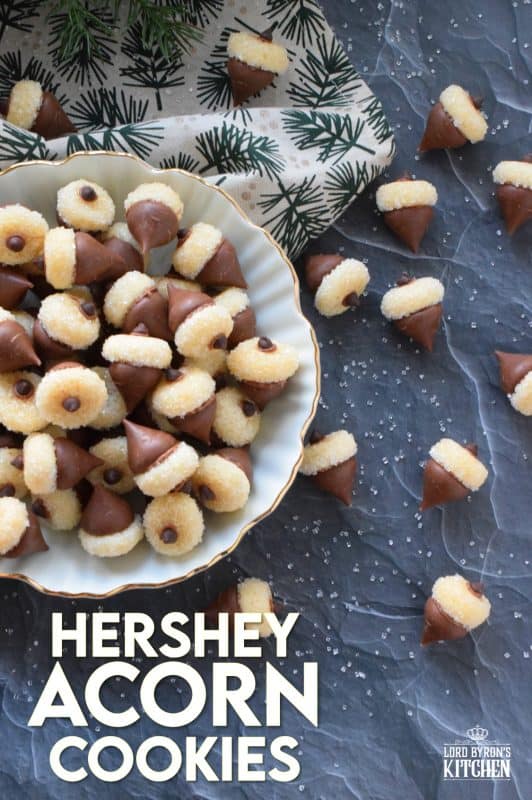 These adorable bite-sized cookies are bound to be a complete hit! They look stunning all on their own, but are perfect for filling in the gaps on your Christmas cookie platter. Hershey Acorn Cookies are prepared with a miniature homemade cookie, and paired with a chocolate kiss and a single chocolate chip! #christmas #holiday #baking #acorn #hershey #kiss #cookies