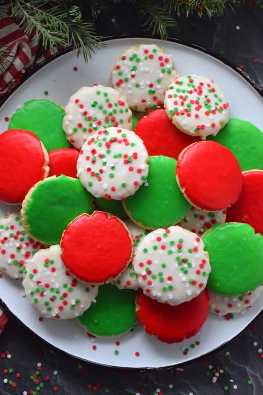 This recipe consists of a melt-in-your-mouth sugar cookie base, topped with a thin, sugary glaze, and festive sprinkles. Holiday Sugar Cookies are brightly and vividly coloured with red and green frosting and will appeal to both the little kids and the big kids in your life! #christmas #holiday #baking #sugarcookies #cookies