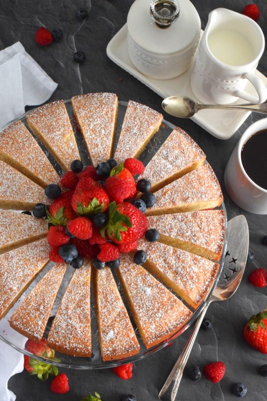 This Bakery Style Vanilla Tea Cake looks superb gussied up with a dusting of confectioner's sugar and a pile of fresh berries. A delightful treat anytime, this cake is the epitome of a beautiful, yet simple, summertime dessert! Bake, slice, and serve with ice cream or whipped cream! #vanillacake #teacake #teatime #bakery