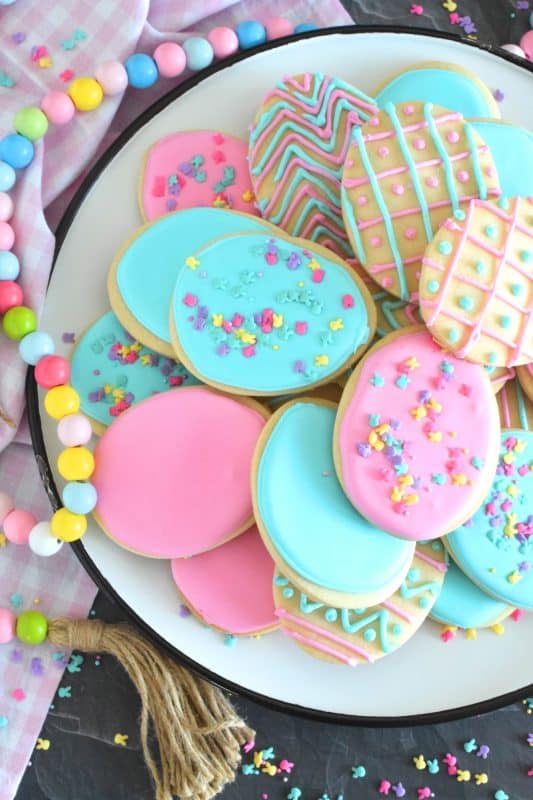 Frosted Easter Egg Cookies are prepared with a light and airy shortbread cookie base consisting of only three ingredients! Once cooled, they are frosted with an easy-to-make royal icing, which hardens and crisps when dried. Topped with sprinkles or simply frosted with whimsical patterns, it's hard to eat only one of these cookies! #easter #easteregg #cookies #royalicing #frosted #sprinkles #cookiecutter