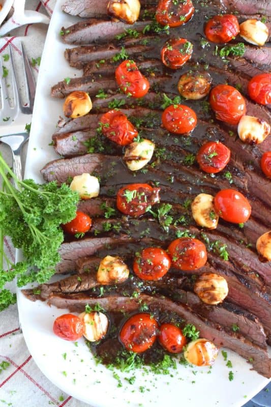 The key to a great tasting flank steak is the marinade. In this recipe, the steak is marinated in olive oil and balsamic vinegar, with mustard, honey, and garlic too. Grilled to your liking and served with blistered tomatoes and melted bocconcini, Grilled Flank Steak Caprese is a quick and easy, family-friendly meal! #flanksteak #beef #steak #grilling #caprese