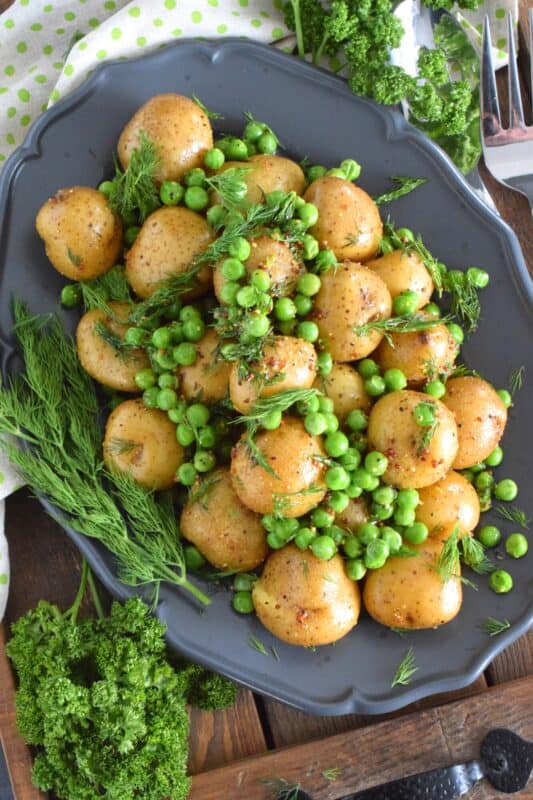 This warm salad consists of pillow-soft baby potatoes, bright green peas, and lots of fresh dill. These are tossed in a dressing prepared with olive oil, grainy mustard, champagne vinegar, and seasonings. Serve this dish anytime, because a really good potato salad is always a hit! #potatosalad #dill #babypotatoes #greenpeas #warmsalad