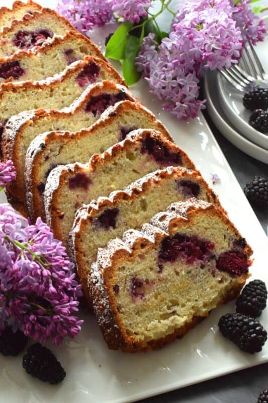 A super moist loaf prepared with fresh blackberries, lemon juice and zest, and hand-picked lilac petals. Not only is this Blackberry Lemon Lilac Loaf delicious and pretty, it is also quite fragrant! If you are fond of the smell of lilacs in early summer, this dessert is sure to please! #edibleflowers #lilacs #loaf #lemon #blackberry #lemonloaf #lilac