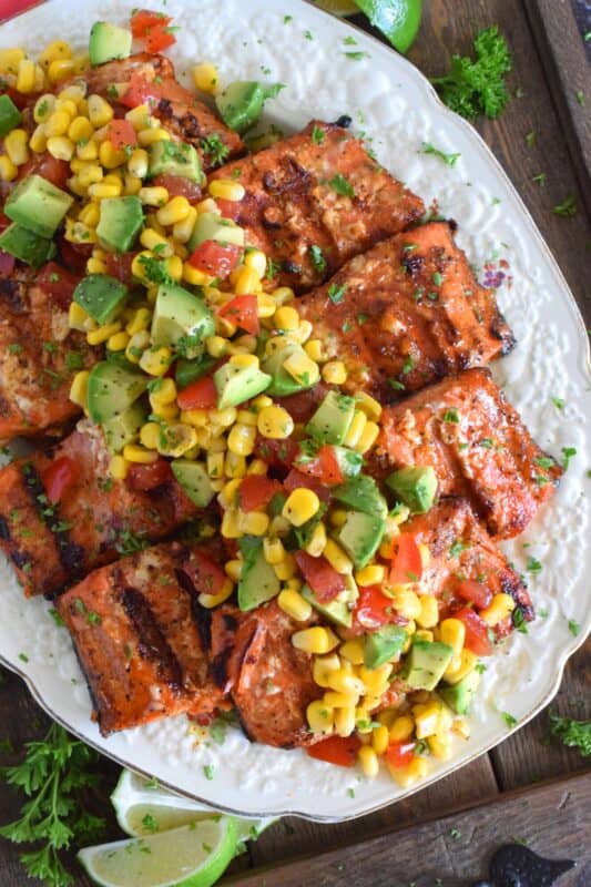 Salmon fillets are marinated in olive oil with honey, lime juice, seasonings, and spices then grilled until charred, yet still light and flaky on the inside. Topped with a salsa consisting of avocado, corn, tomatoes, and lime, this grilled salmon is not only refreshing and delicious, but also quite a beautiful and impressive main for you and your family this summer! #salmon #grillesalmon #chililime #salsa #summermeals #grilled #seafood