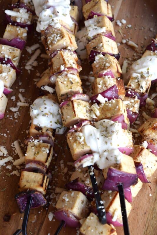 Extra firm tofu is marinated with red onion in a mixture of olive oil and the best quick and easy homemade Greek seasoning.  Grilled until slightly charred and topped with tzatziki and crumbled feta, these skewers are a great grilled meat alternative! #grilledtofu #tofu #greekrecipes #vegetarian #summergrilling