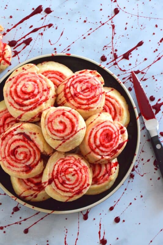 Despite their horror-ish name and their bloody demeanour, Jigsaw Pinwheel Cookies are a light and buttery delight! Liberally dusted with red sanding sugar, the biscuit-like dough is rolled to form the look of Jigsaw's red and white spirally cheeks. Complete with a splattering of homemade edible blood, these cookies are perfect for Halloween and the Saw franchise fan! #jigsaw #saw #sawmovie #halloween #cookies #edible #blood