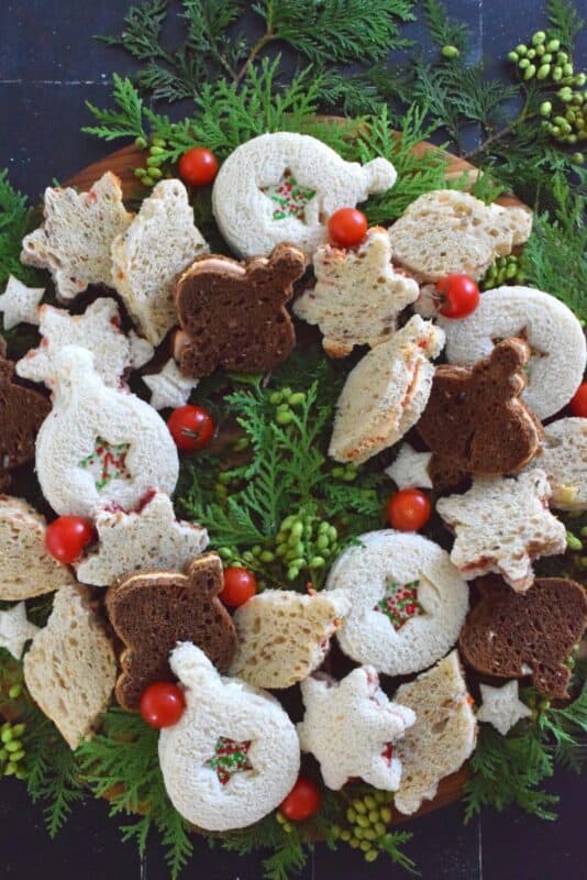 The sandwiches that make up this Holiday Sandwich Wreath are small, delicious, and festively shaped with your favourite cookie cutters. With four different flavours, there's one for everyone! Serve these finger sandwiches with a cup of hot tea at an afternoon holiday gathering! #sandwiches #fingerfoods #charcuterie #christmas #holiday #nobake