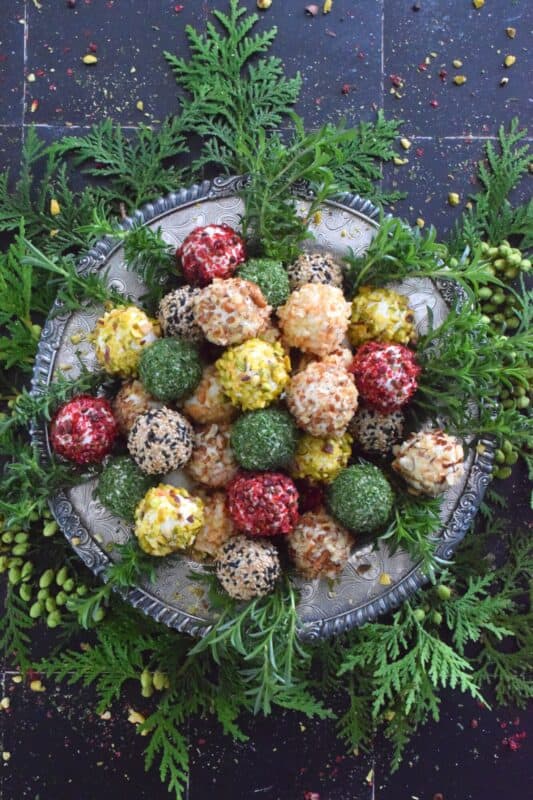 These little balls of cheese are rolled in a variety of toppings like toasted nuts and sesame seeds, dried herbs, and even some crushed pink peppercorns for some heat! A Holiday Cheese Ball Wreath is a great way to jazz up your snack table! Serve with your favourite crackers and some warm crostini! #christmas #holiday #appetizer #cheese #platter