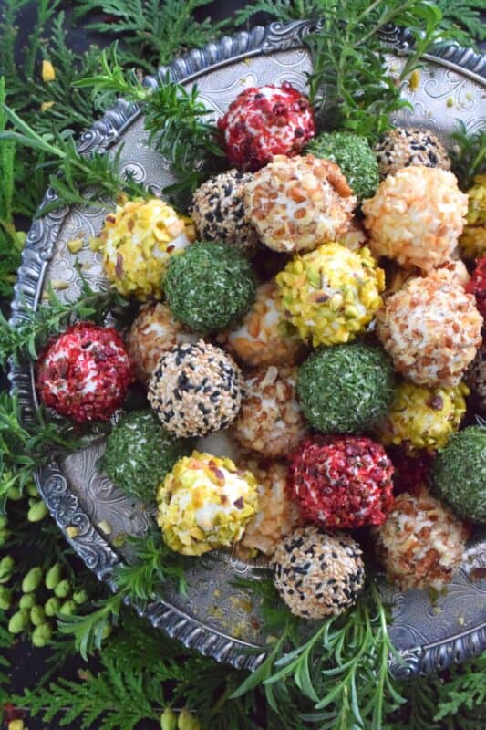 These little balls of cheese are rolled in a variety of toppings like toasted nuts and sesame seeds, dried herbs, and even some crushed pink peppercorns for some heat! A Holiday Cheese Ball Wreath is a great way to jazz up your snack table! Serve with your favourite crackers and some warm crostini! #christmas #holiday #appetizer #cheese #platter