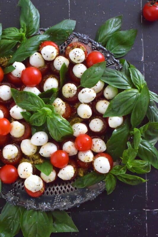 Simple, sweet, and cheesy!? You bet! This gorgeous Festive Caprese Wreath is easily prepared with hollowed-out cherry tomatoes stuffed with basil pesto and mini bocconcini. Sprinkle over some freshly ground black pepper, drizzle with olive oil, and tuck in some fresh basil leaves before serving! #festive #caprese #ediblewreath #tomatoes #bocconcini