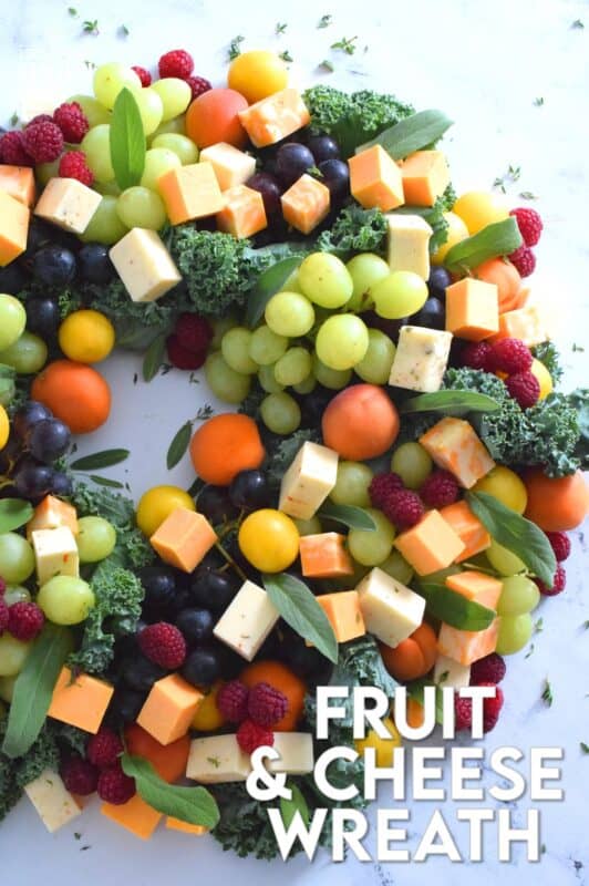 An edible wreath consisting of red and green grapes, fresh apricots, tart plums, vibrantly red raspberries, and various types of cheese, this beautifully festive Fruit and Cheese Wreath is a wonderful way to display and serve your guests this holiday season! #christmas #holiday #fingerfoods #appetizers #cheeseplatter #charcuterie #grazing #board
