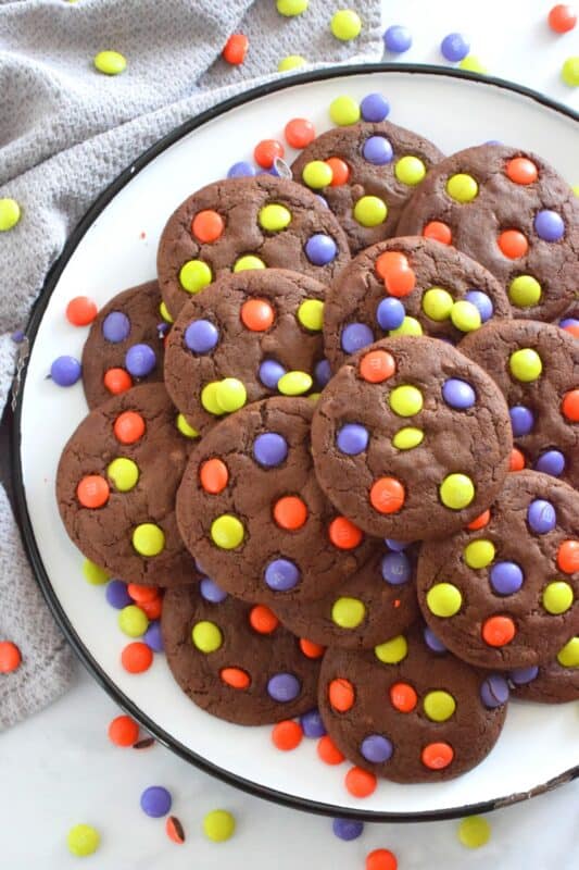 Chocolate Halloween Cookies have a slightly crispy exterior with a dense chocolaty center. Stuffed with white chocolate chips and topped with green, purple, and orange M&M candy, these cookies are both delicious and festive!  Your little trick-or-treaters are going to love these! #m&m #halloween #cookies #chocolate #trickortreat