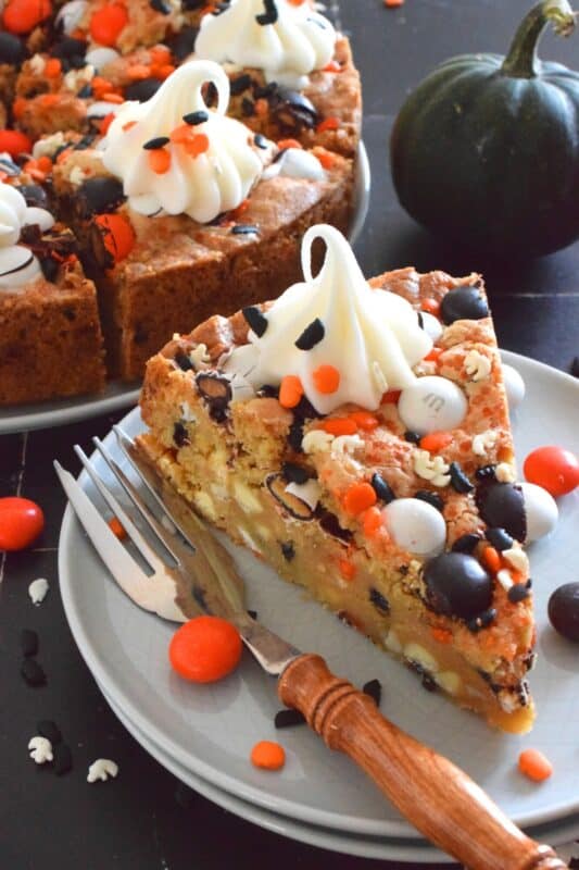 One giant cookie that eats like a cake, this M&M Cookie Cake is perfect when served with a dollop of frosting on each slice. Loaded with candy-coated chocolate and autumn sprinkles, this cake is a fun dessert the whole family will love! #M&M #halloween #cookie #cake #chocolate