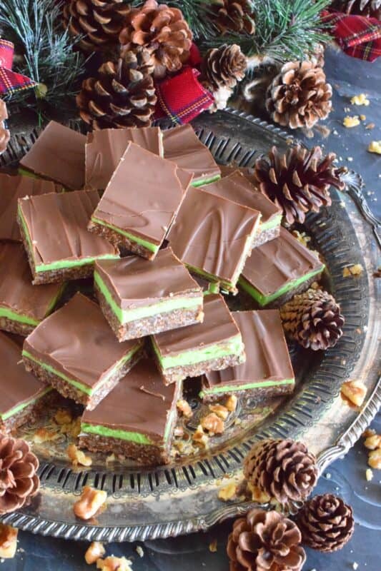 Triple-layered with wonderful flavours, these No Bake Mint Squares are perfectly festive for the holiday season.  With a coconut, walnut, and graham crumb base, and a creamy mint filling, these squares are topped with melted chocolate which makes them all the more rich and delicious.  You simply must add these to your Christmas cookie platter! #nanaimo #mint #peppermint #squares #bars #nobake