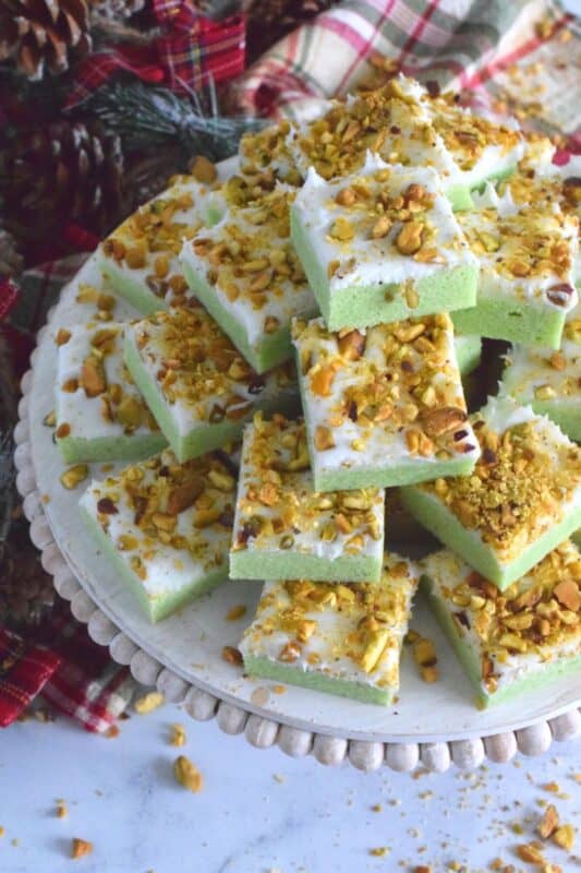 The uncomplicated and delicious sugar cookie gets a fresh, new flavour profile, and an upgrade in this Pistachio Sugar Cookie Squares recipe.  The classic sugar cookie base is pistachio flavoured and prepared with boxed pistachio pudding powder.  Topped with a layer of delicious buttercream frosting and sprinkled with roasted, salted chopped pistachios, this cookie is simply irresistible! #pistachio #sugarcookies #cookies #christmas #holiday #squares #baking