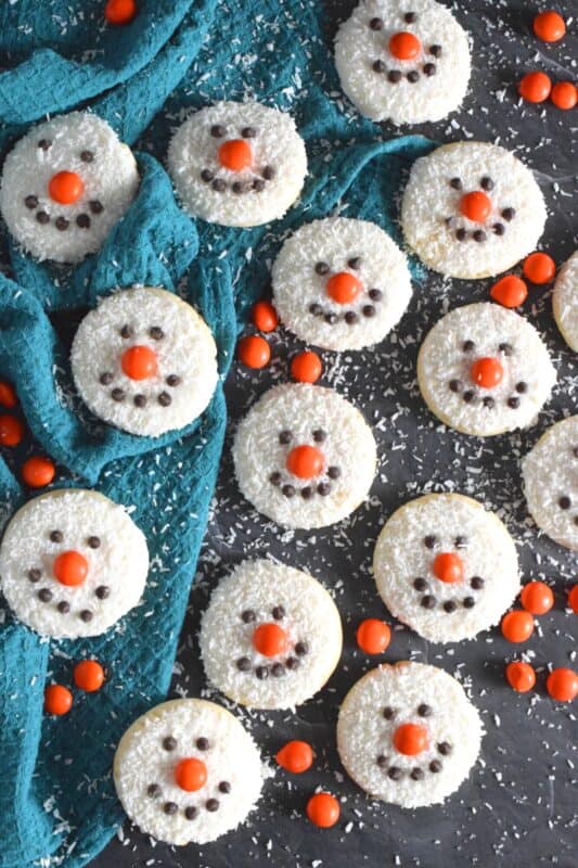 Coconut Snowman Cookies are simply adorable! They're also very easy to make, inexpensive, and delicious too! The base of the cookie melts in your mouth! Using mini chocolate chips for his eyes and mouth, and an orange candy-coated chocolate for his nose, these cookies are almost too cute to eat! #snowman #coconut #cookies #sugarcookies