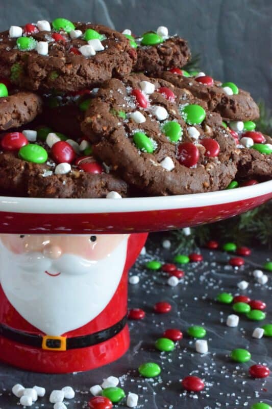 Holiday Trash Cookies are loaded with both milk and white chocolate chips, M&Ms, crushed pretzels, and marshmallow bits too! The cookie dough is prepared with brown sugar, which means these cookies are soft and moist on the inside, but they have a crisp exterior! Make a delightfully tasty gift by packaging these festive cookies up in boxes and tying them with a bright festive ribbon! #mandm #christmas #santa #cookies #trash