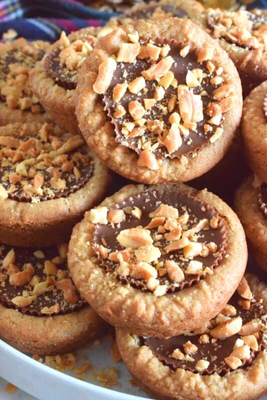 Thumbprint-style cookies are very popular at Christmastime, so why not over-stuff them with a full-sized Peanut Butter Cup? These cookies are so easy to make and are baked in muffin tins! Push in the peanut butter cup and top with chopped peanuts for more texture and flavour! #peanutbutter #reeses #cookies #thumbprint