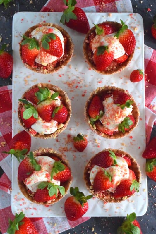 Sugary sweet and crunchy waffle bowls are coated with strawberry shortcake crumbs and filled with a light and fluffy cheesecake mixture, topped with fresh strawberries, and more strawberry shortcake crumbs. This gorgeously impressive dessert is for the serious strawberry lover! #shortcake #waffle #strawberry #cheesecake