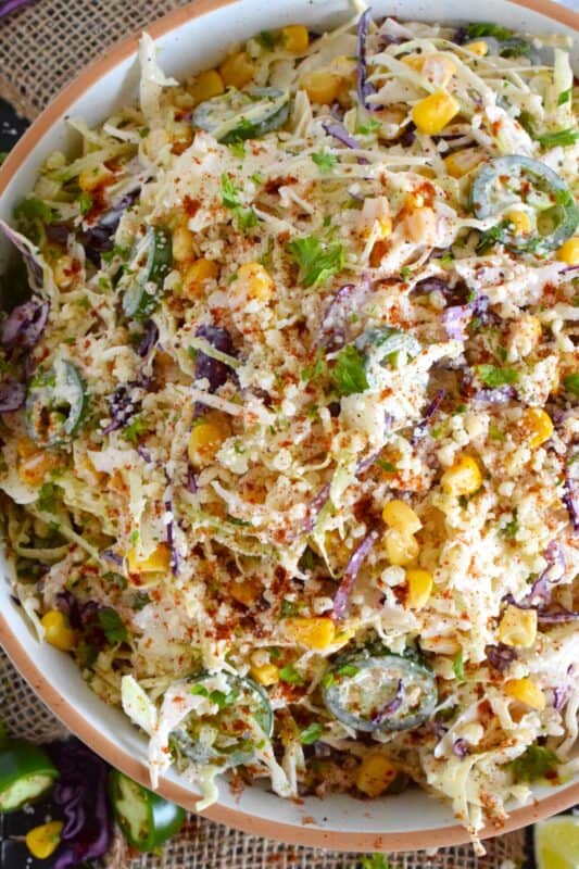 Crisp red and green cabbage, sweet corn, spicy jalapenos, fresh green onions, and salty cotija cheese all meet in the middle to create this most delicious Mexican Street Corn Coleslaw. With its creamy, zingy, and tart dressing, this coleslaw will most definitely please the toughest critic! #mexican #streetcorn #coleslaw #salad