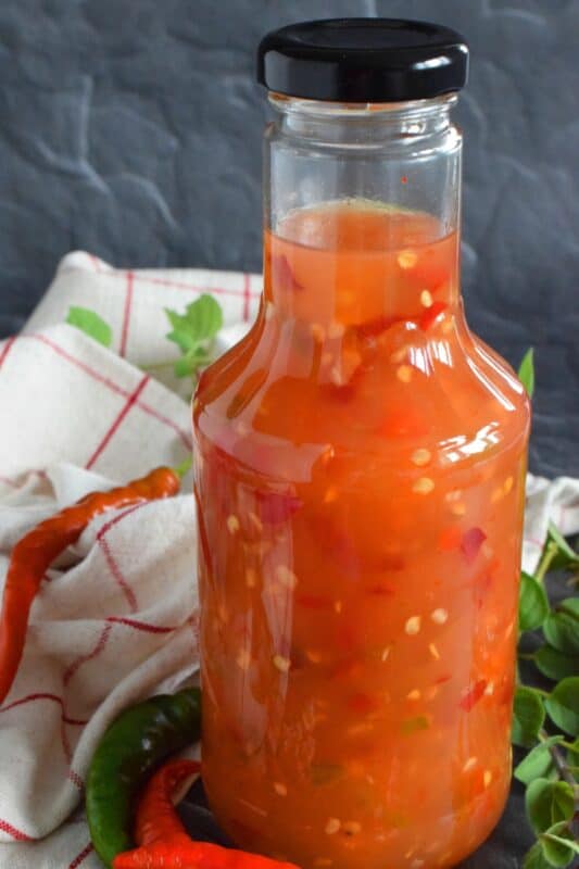 This hot and spicy sauce is not super hot, especially not in smaller amounts. Making good use of the last of the peppers before the frost hits is what this recipe was made for. Flecked with both red and green chilies, this sauce has so many uses! Prepared with vinegar, garlic, sugar, and salt, the flavour profile is complex and layered! #cayenne #pepper #sauce #canning #waterbath