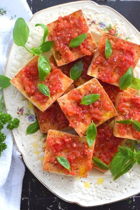 Summer fresh tomatoes are peeled and mashed and spread onto warm, toasted bread that has been rubbed with whole garlic cloves. Seasoned with ground black pepper and flaked sea salt, and a splash of olive oil, Spanish Tomato Bread is a popular tapas bar recipe! #catalan #spanish #tomato #bread