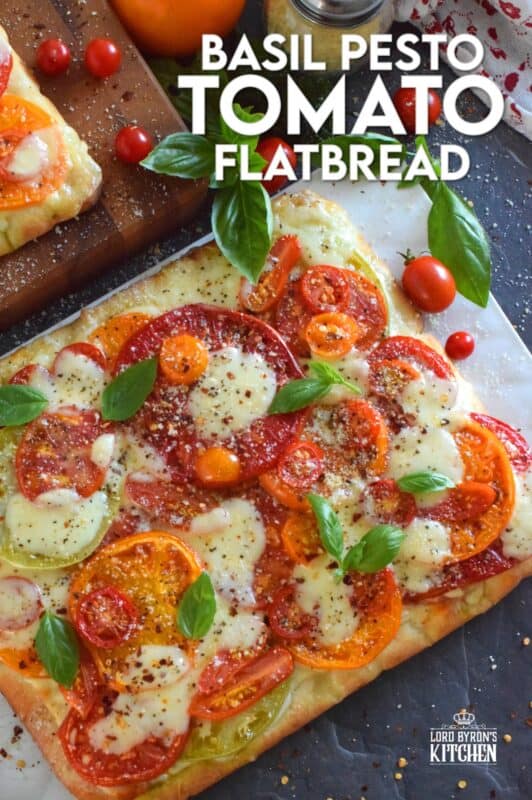 Freshly sliced tomatoes and cheese are piled onto a quick and easy homemade flatbread with the best double parmesan basil pesto sauce. Baked to perfection and topped with fresh basil leaves and ground black pepper, this is a very scrumptiously delicious recipe! #tomatoes #flatbread #heirloom #summerfresh