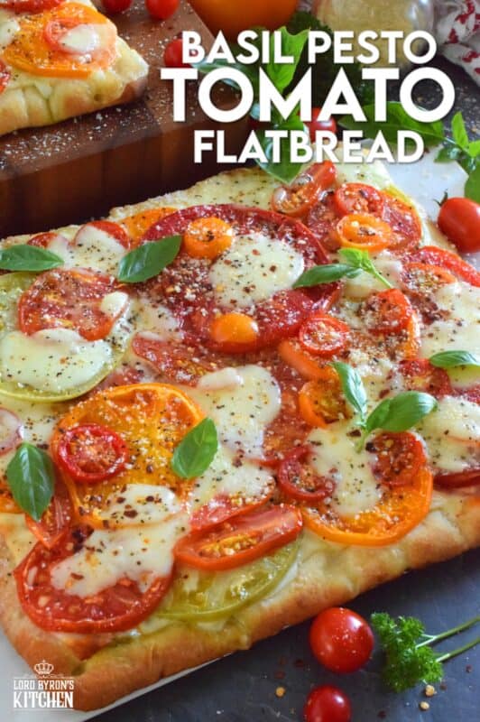 Freshly sliced tomatoes and cheese are piled onto a quick and easy homemade flatbread with the best double parmesan basil pesto sauce. Baked to perfection and topped with fresh basil leaves and ground black pepper, this is a very scrumptiously delicious recipe! #tomatoes #flatbread #heirloom #summerfresh