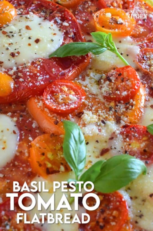 Freshly sliced tomatoes and cheese are piled onto a quick and easy homemade flatbread with the best double parmesan basil pesto sauce. Baked to perfection and topped with fresh basil leaves and ground black pepper, this is a very scrumptiously delicious recipe! #tomatoes #flatbread #heirloom #summerfresh