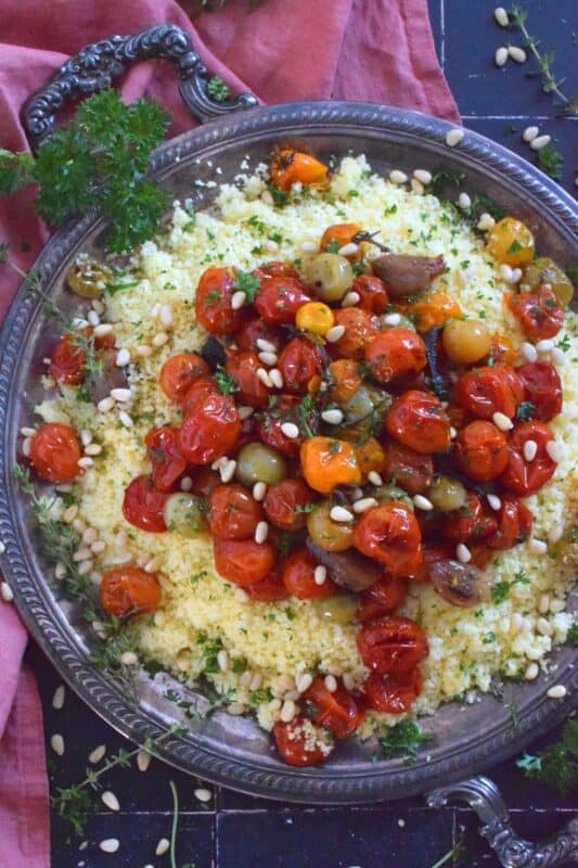 Summer fresh cherry tomatoes are slowly roasted with garlic, onions, and herbs in olive oil until the skins have blistered. Spoon over cooked couscous and sprinkle with pinenuts for a delicous, comforting, and filling main or side! #couscous #confit #tomato #roasted