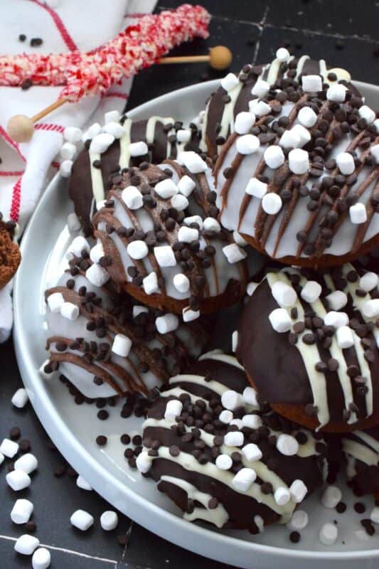 Good cocoa is the secret to a decadent hot chocolate; the same can be said for these Hot Chocolate Donuts.  Marshmallows are baked into the chocolate donut and sprinkled on top of the white glaze and the chocolate drizzle.  These baked donuts are for the ultimate chocolate lover! #hotchocolate #donuts #marshmallows