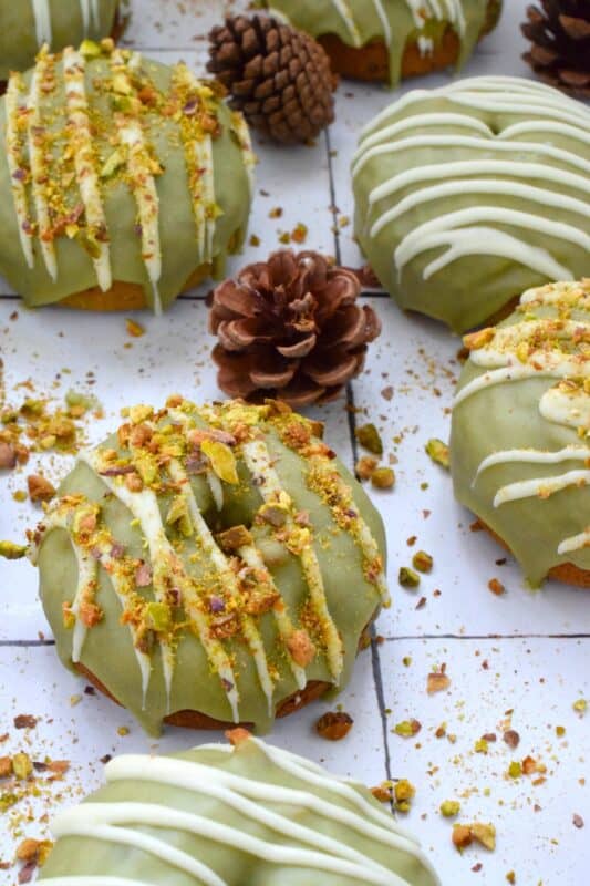 Everything is coming up green in these Matcha Pistachio Donuts! The batter is light and fluffy and prepared with finely chopped pistachios and matcha. Dipped in matcha-infused icing and drizzled with white chocolate, these donuts are delicious and addictive! #matcha #greentea #donuts #pistachio