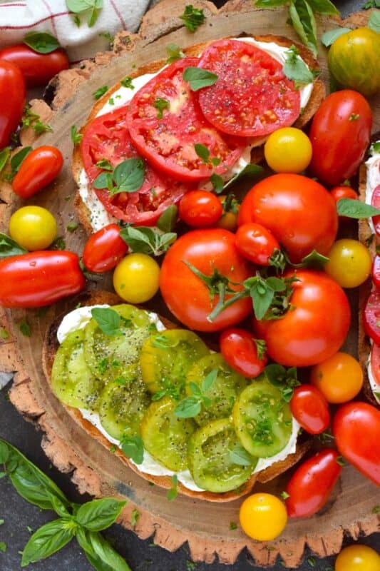 Summer fresh tomatoes are piled onto lightly toasted bread with a generous spread made with cream cheese. Tomato Cream Cheese Toast is a delicious summertime lunch or an appetizer too! Don't forget to season the tomatoes well and use fresh herbs for flavour and garnish. #sandwich #tomato #openfaced #creamcheese