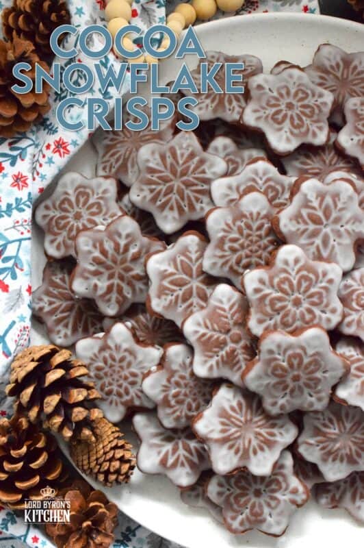 These thin and crispy chocolate cookies are a perfect holiday treat! Cocoa Snowflake Crisps are made with good cocoa and salted butter which help to make them super chocolatey and buttery with a snap-crisp texture. Top them with a thin sugary glaze to make them extra tasty and super festive too! #cocoa #chocolate #snowflake #cookies