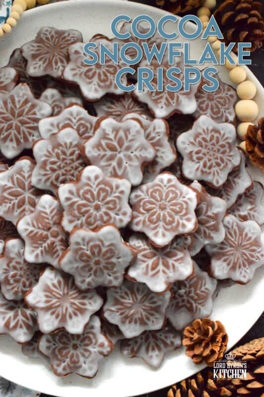 These thin and crispy chocolate cookies are a perfect holiday treat! Cocoa Snowflake Crisps are made with good cocoa and salted butter which help to make them super chocolatey and buttery with a snap-crisp texture. Top them with a thin sugary glaze to make them extra tasty and super festive too! #cocoa #chocolate #snowflake #cookies