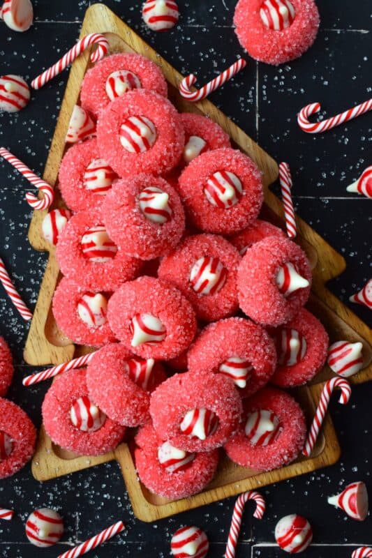 A deliciously decadent peppermint cookie, coated in sugar, and topped with a Hershey's white chocolate kiss, Candy Cane Hershey Kiss Cookies are a perfect holiday treat that everyone will love! These are quick and easy – no need to chill the cookie dough before baking either! Don't they look absolutely adorable!? #thumbprint #hershey #kisses #candycane