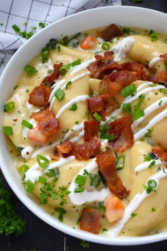 Bacon and Pierogi Soup starts with crispy, fried bacon being tossed with fragrant rosemary. Next, aromatic vegetables like carrots, onions, and celery are added to the pot with garlic and thyme. Frozen pierogies are added and cooked in a thick soup with shredded cheese. Ladle up a big bowl and top it with that rosemary-infused bacon, sour cream, and more cheese. #soup #pierogi #bacon