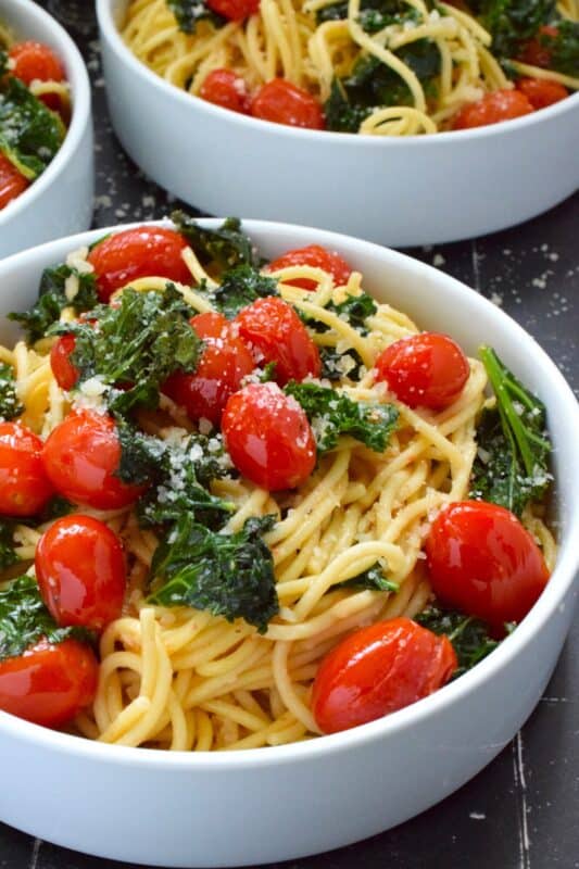 Love it or hate it, kale is an economical and delicious way to get more nutrient-dense goodness into a comforting bowl of pasta like in the case of this Tomato and Kale Spaghetti! Saute the kale in butter with garlic and shallots to make a delicious and aromatic start to this dish. Garnish with salty, nutty, grated parmesan and dig into this healthy and hearty dinner! #spaghetti #pasta #kale #vegetarian #cheesy #tomatoes
