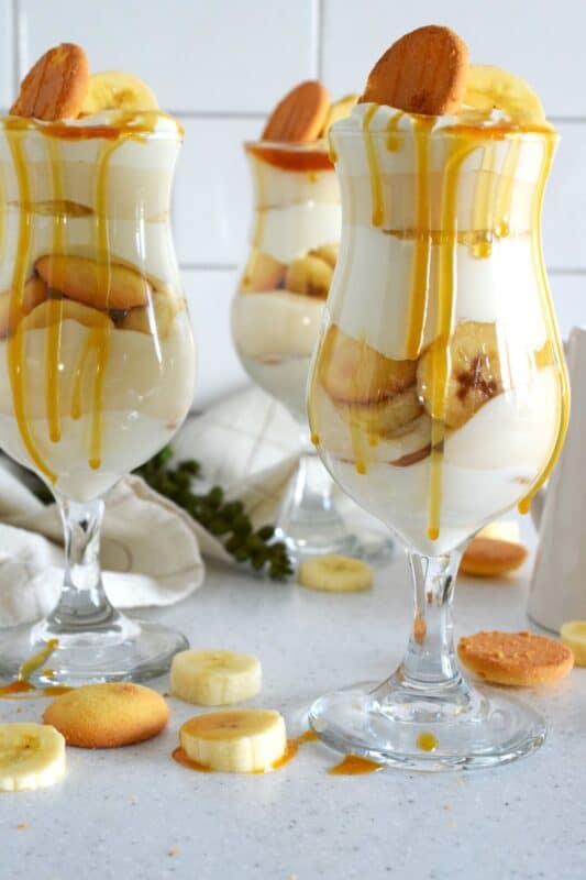 Layers of vanilla wafer cookies, homemade mascarpone cream, banana pudding, and freshly sliced bananas, these parfaits are quick and easy to make! Serve them family style or fancy them up by serving them in these individual glasses. Top with whipped cream and an optional caramel drizzle. They're a feast for the eyes! #banana #pudding #parfait #nobake #layered #dessert
