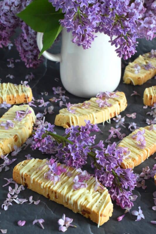 These biscotti are loaded with lilac flavour and scent.  Lilac petals are incorporated into the biscotti dough which has been sweetened with homemade lilac sugar.  Glazed and topped with more lilacs, these Lilac Blossom Biscotti are light, airy, and delicious! Super easy to make, and with their cheerful inclination, no one could resist! Treat yourself to one of these with a hot tea on a lazy Sunday afternoon. #lilac #biscotti #flowers #petals #brunch