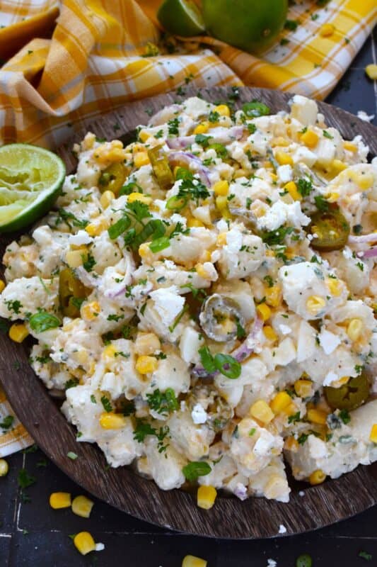Chopped potatoes are tossed with sweet corn, spicy jalapenos, boiled eggs, fresh green and red onions, and salty cotija cheese to create this most delicious Mexican Street Corn Potato Salad! With its creamy, zingy, and tart dressing, this potato salad will most definitely be the most popular side at any backyard barbecue this summer! #salad #potato #streetcorn #mexican #cotija