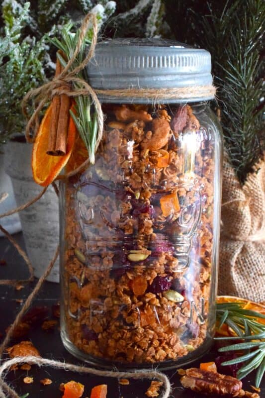 Almonds, cashews, pecans, pumpkin seeds, cranberries, and apricots help to flavour and bulk up this Holiday Gingerbread Granola. Baked with maple syrup and butter, and seasoned with cinnamon, nutmeg, and allspice, this healthy snack makes a very delicious giftable treat! #granola #homemade #gift #gingerbread