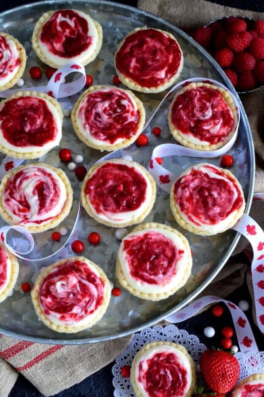 An easy to assemble treat perfect for any Canada Day celebration. Red Berry Swirl Tartlets are flaky, buttery, creamy, and sweet. Buy store-bought frozen tart shells to make this recipe fast and easier. These are stuffed with a cream cheese filling and a red berry compote! #tarts #tart #berry #tartlets
