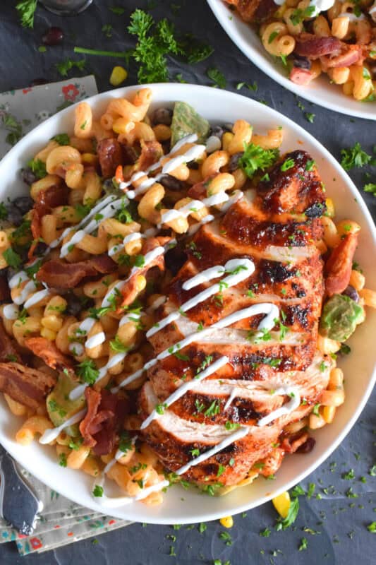 Spice-seasoned chicken breasts are grilled to perfection and then brushed with BBQ sauce and served with a delicious pasta salad prepared with bacon, avocado, corn, black beans, green onions, and roasted red peppers.  This pasta salad dinner is a hearty meal great for any backyard family picnic! #bbq #chicken #pasta #salad #dinner